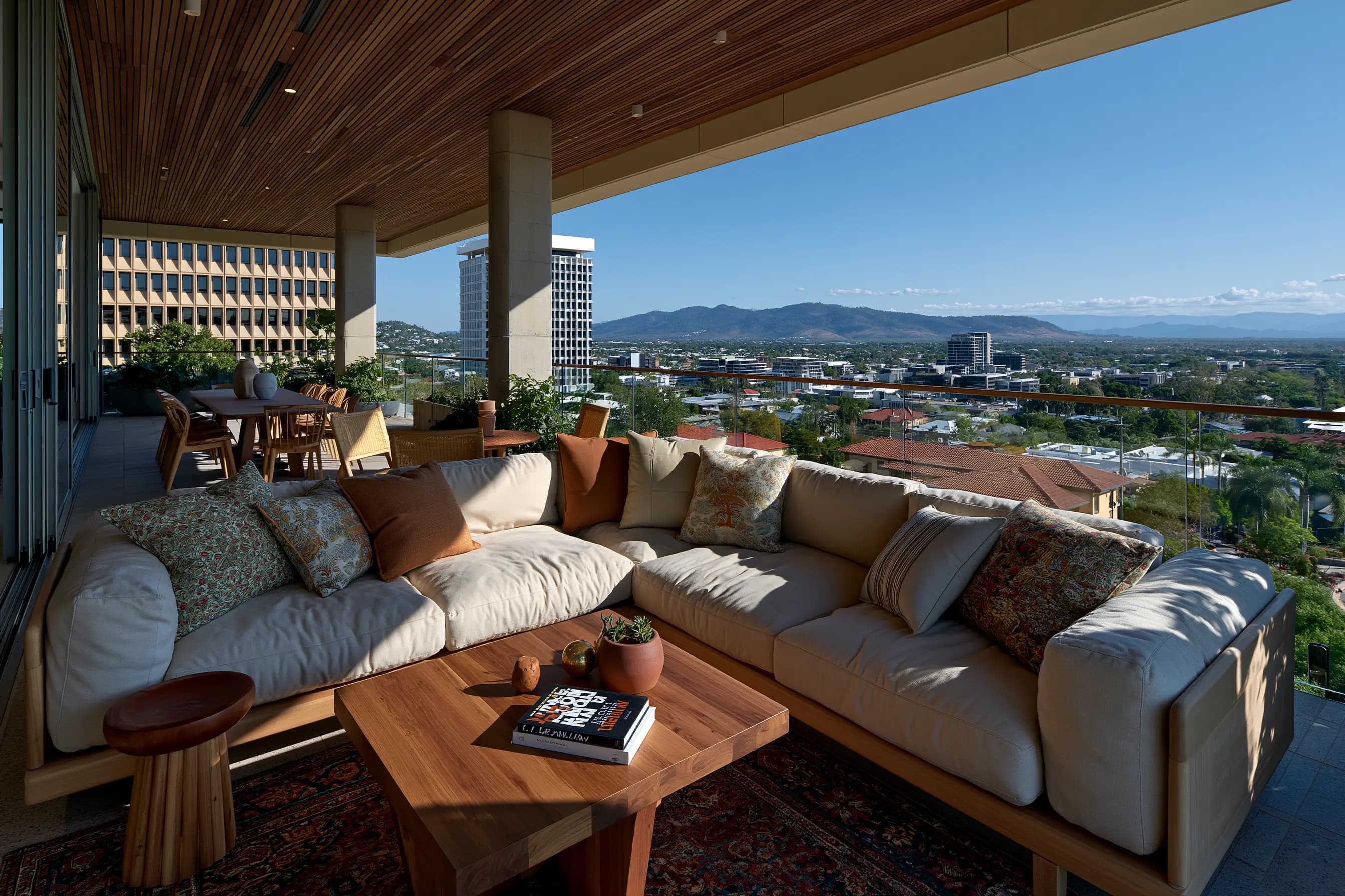 Covered rooftop lounge with a cream sectional sofa and wooden coffee table overlooking a city skyline and mountains