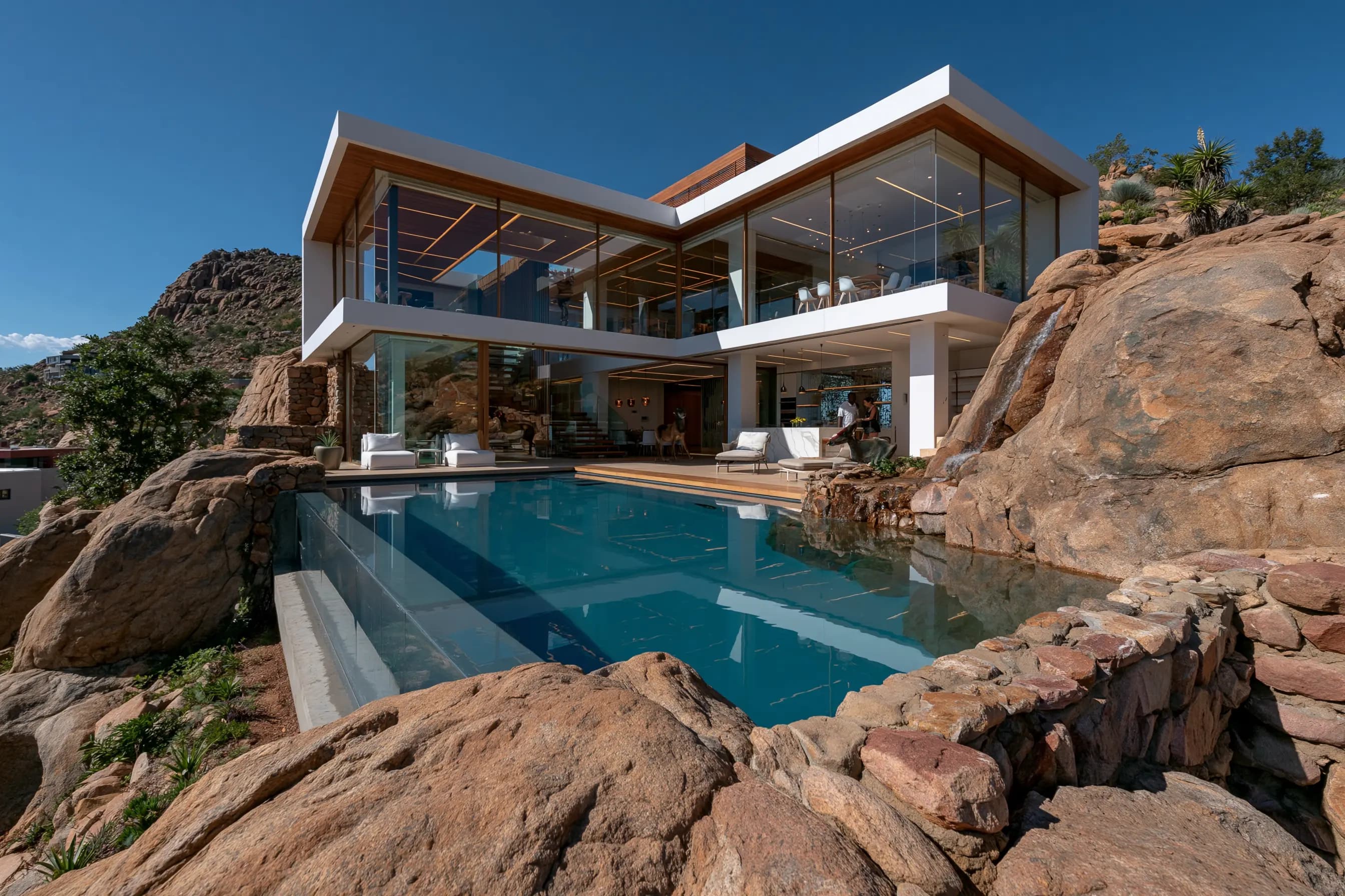 Glass-walled contemporary home built into a rocky hillside with a cascading pool